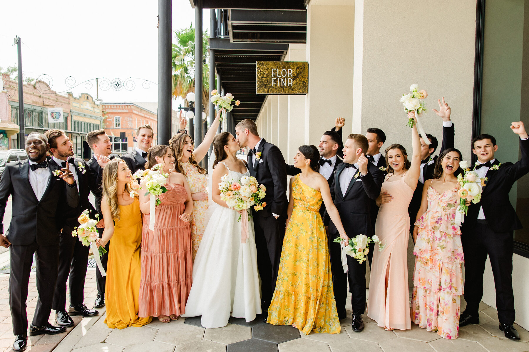 Bride and groom sharing a kiss as their colorful bridal party cheers outside in Ybor City, Tampa — luxury wedding photographer Ailyn La Torre