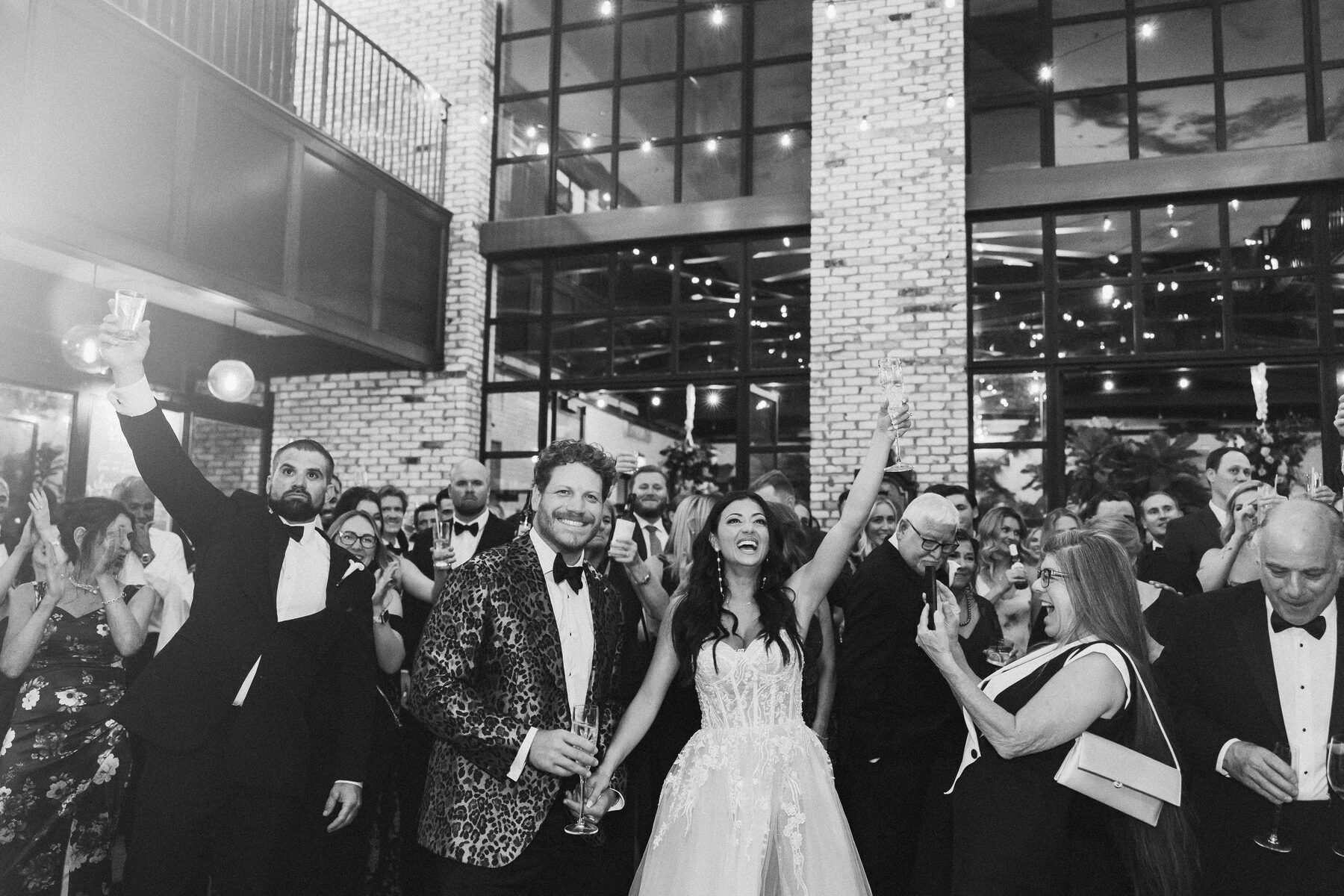 Groom in a bold leopard print tuxedo and bride in an embellished ballgown raising glasses to celebrating guests at the Oxford Exchange in Tampa — luxury wedding photographer Ailyn La Torre
