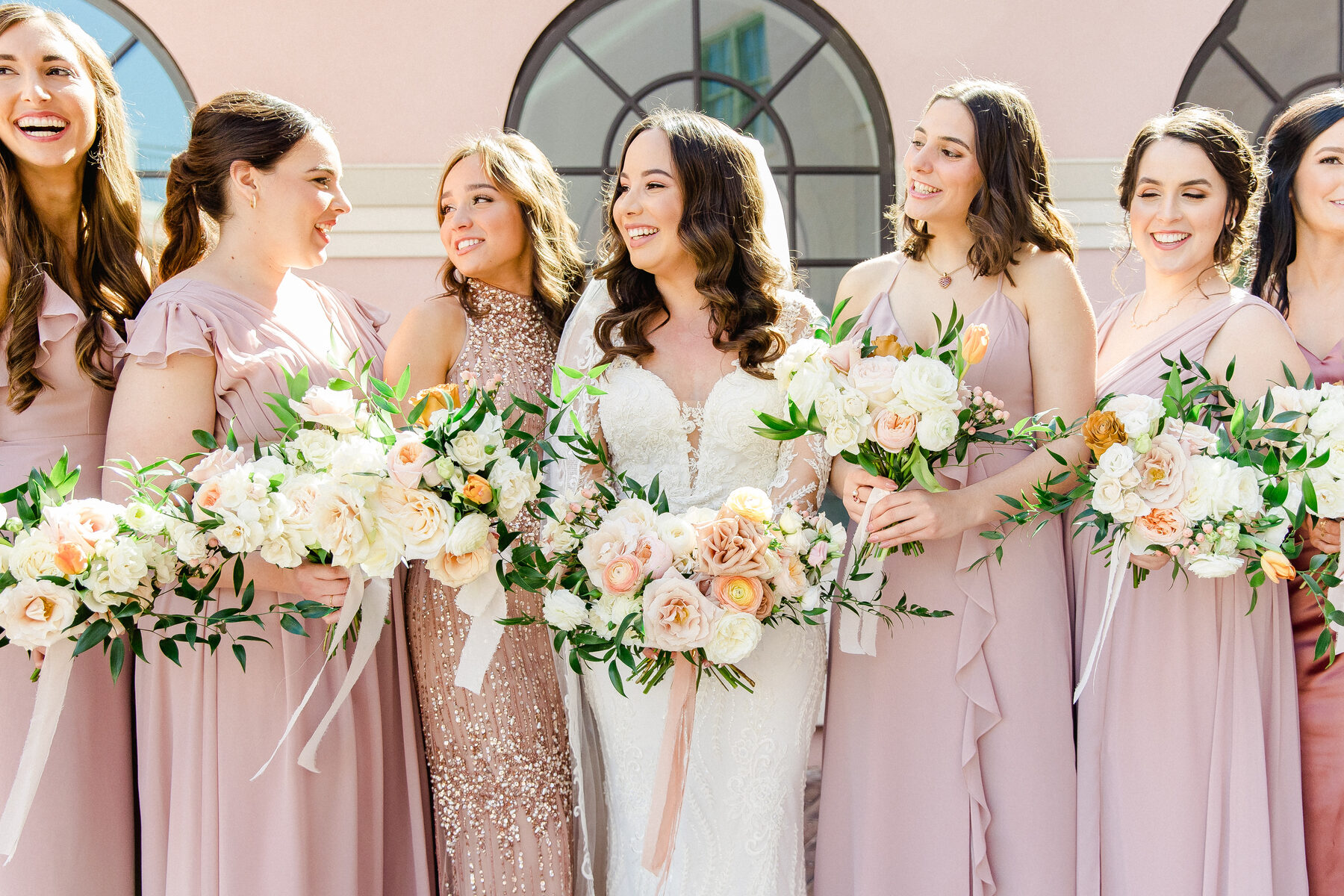 Bride laughing with her bridesmaids in dusty rose gowns outside the Vinoy in St. Petersburg, each holding a lush peach and white bouquet — luxury wedding photographer Ailyn La Torre
